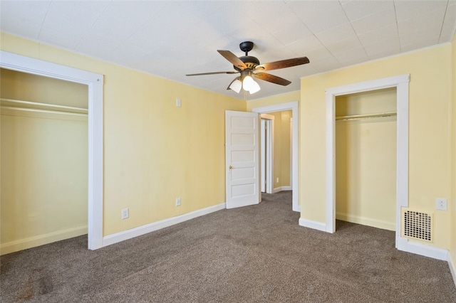 unfurnished bedroom with ceiling fan, two closets, and dark carpet