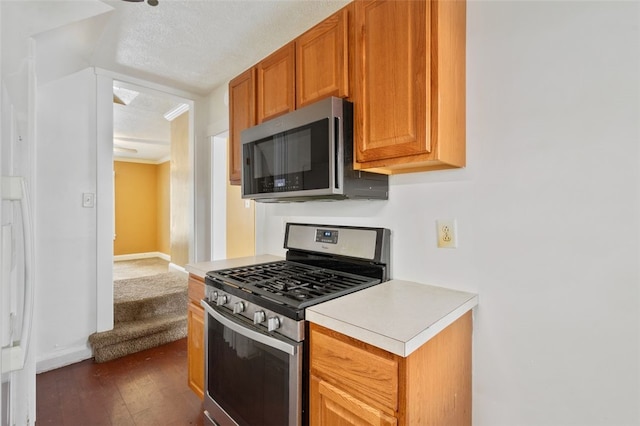 kitchen featuring dark wood-type flooring, appliances with stainless steel finishes, a textured ceiling, and ornamental molding