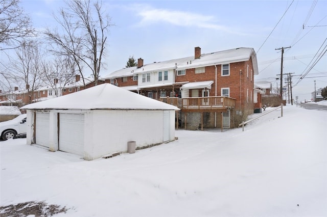 snow covered back of property with a garage, an outbuilding, and a wooden deck