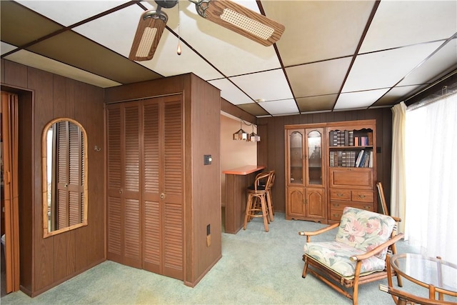 sitting room with light carpet, a paneled ceiling, ceiling fan, and wood walls