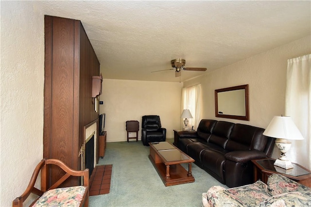 living room with ceiling fan, light colored carpet, a textured ceiling, and a fireplace