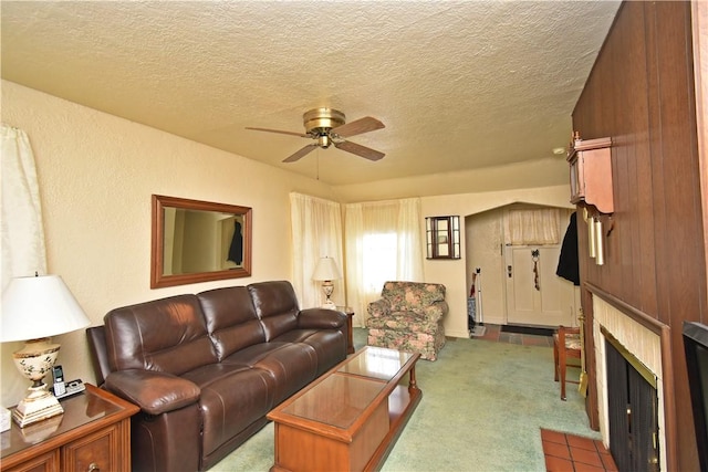 carpeted living room featuring ceiling fan, a tiled fireplace, and a textured ceiling