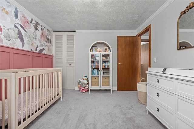 bedroom featuring a textured ceiling, a closet, light colored carpet, a nursery area, and crown molding