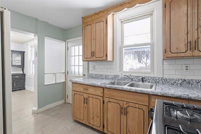 kitchen with light wood-type flooring, decorative backsplash, gas range oven, and sink