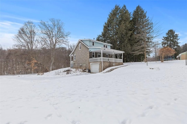 snow covered back of property with covered porch and a garage