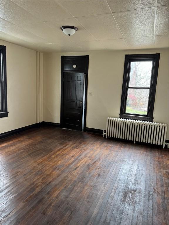 spare room with dark hardwood / wood-style floors and radiator heating unit