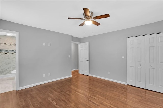 unfurnished bedroom with ceiling fan, a closet, connected bathroom, and wood-type flooring