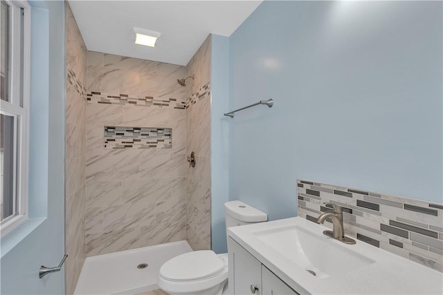 bathroom featuring toilet, decorative backsplash, a tile shower, and vanity