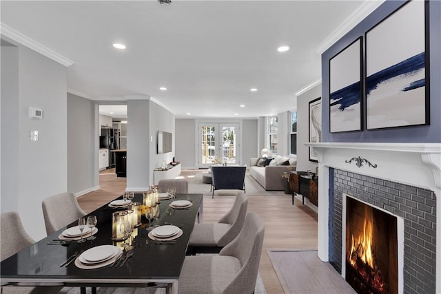 dining space with a tile fireplace, ornamental molding, french doors, and light wood-type flooring