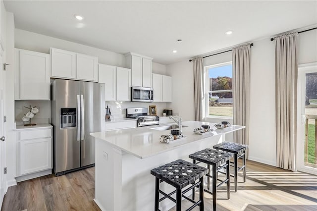 kitchen with sink, white cabinetry, stainless steel appliances, light hardwood / wood-style floors, and an island with sink