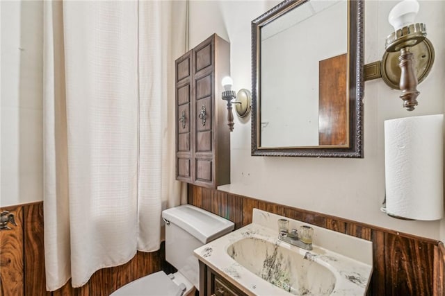 bathroom with toilet, wooden walls, and vanity