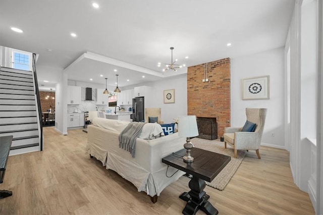 living room with light wood-type flooring, a brick fireplace, sink, and a notable chandelier