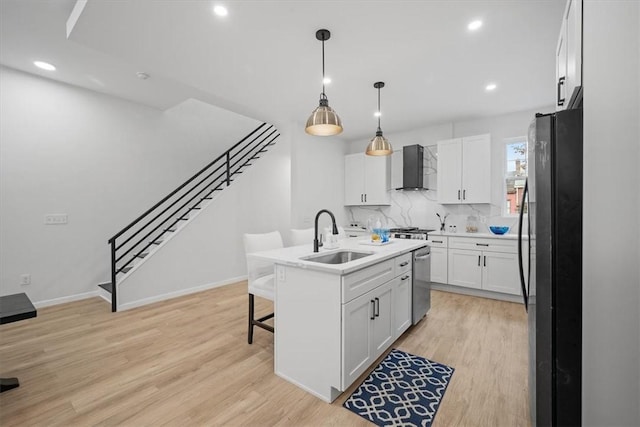 kitchen featuring a center island with sink, sink, white cabinetry, black refrigerator, and wall chimney exhaust hood