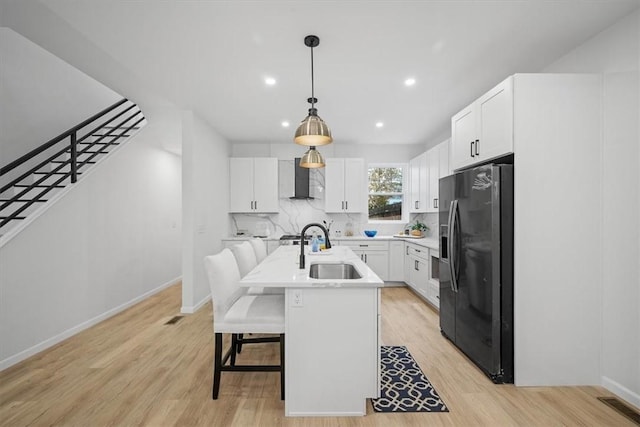 kitchen with sink, an island with sink, white cabinets, and black fridge with ice dispenser