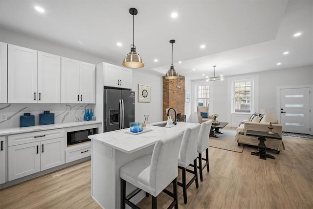 kitchen with white cabinets, stainless steel fridge, and an island with sink