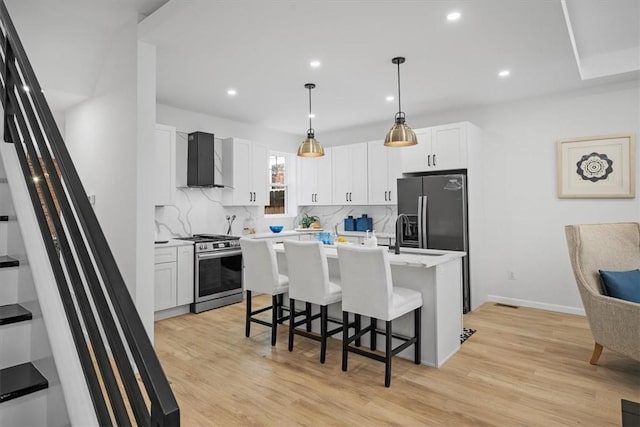 kitchen featuring white cabinetry, a center island with sink, stainless steel range with gas stovetop, backsplash, and wall chimney exhaust hood