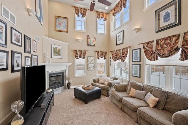 living room with ceiling fan, plenty of natural light, a high end fireplace, and a towering ceiling