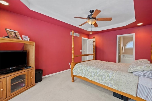 carpeted bedroom featuring a raised ceiling, ceiling fan, and connected bathroom