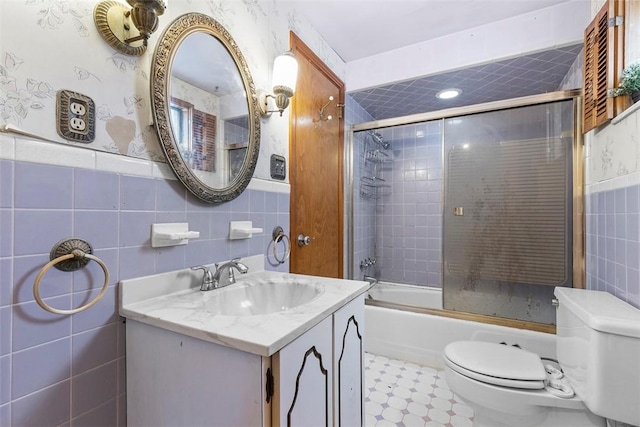 full bathroom featuring toilet, bath / shower combo with glass door, tile walls, and vanity