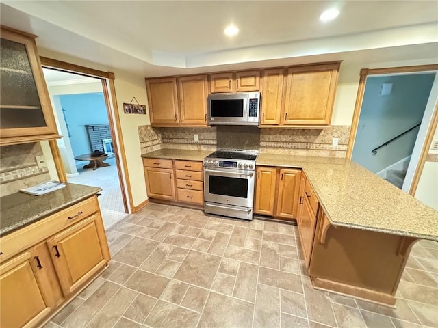 kitchen featuring backsplash, appliances with stainless steel finishes, kitchen peninsula, and a breakfast bar area