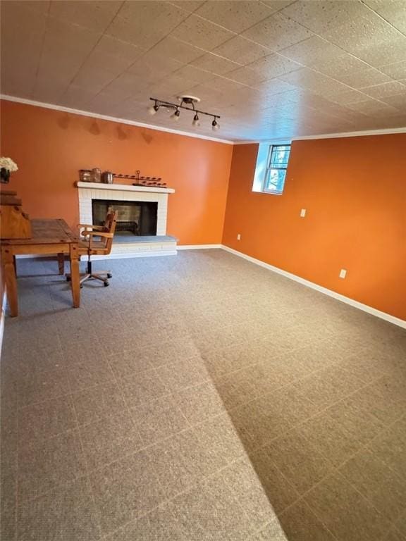 basement with a brick fireplace, ornamental molding, rail lighting, and carpet