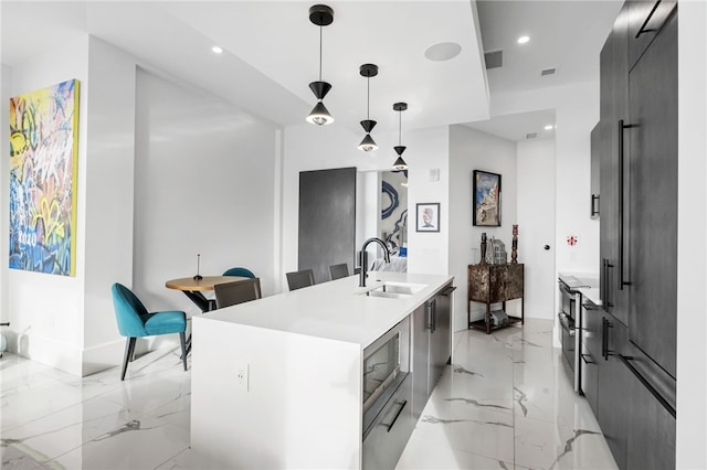 kitchen with hanging light fixtures, stainless steel microwave, sink, and a center island with sink