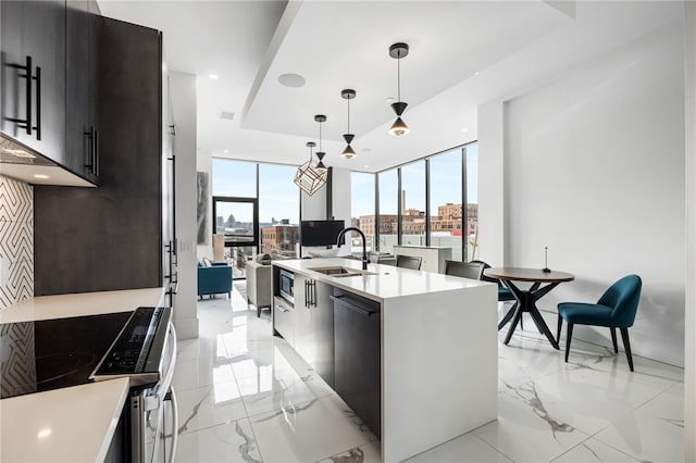 kitchen with a center island with sink, electric range, sink, hanging light fixtures, and a wall of windows