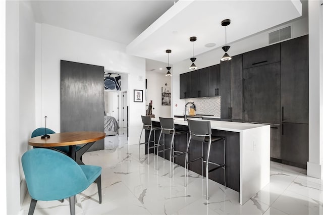 kitchen with an island with sink, a breakfast bar area, backsplash, decorative light fixtures, and sink