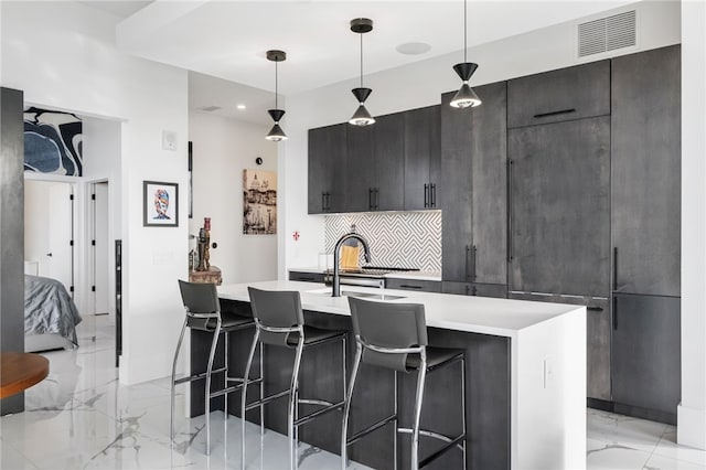 kitchen with a center island with sink, tasteful backsplash, a kitchen breakfast bar, hanging light fixtures, and sink