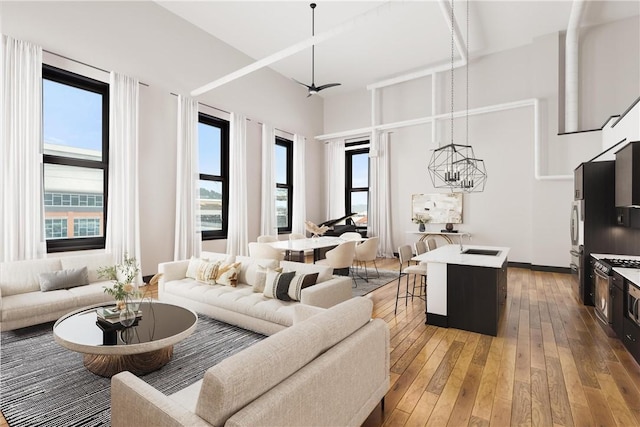 living room featuring wood-type flooring, a towering ceiling, sink, and ceiling fan with notable chandelier