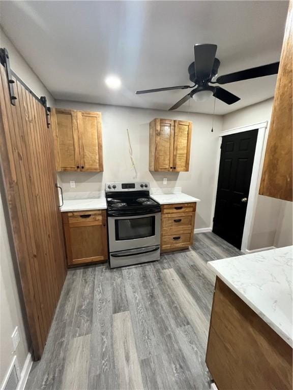 kitchen featuring wood-type flooring, a barn door, ceiling fan, and stainless steel electric range oven