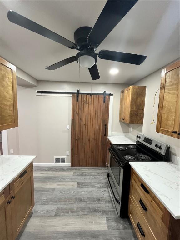 kitchen with stainless steel range with electric cooktop, a barn door, wood finished floors, a ceiling fan, and light stone countertops