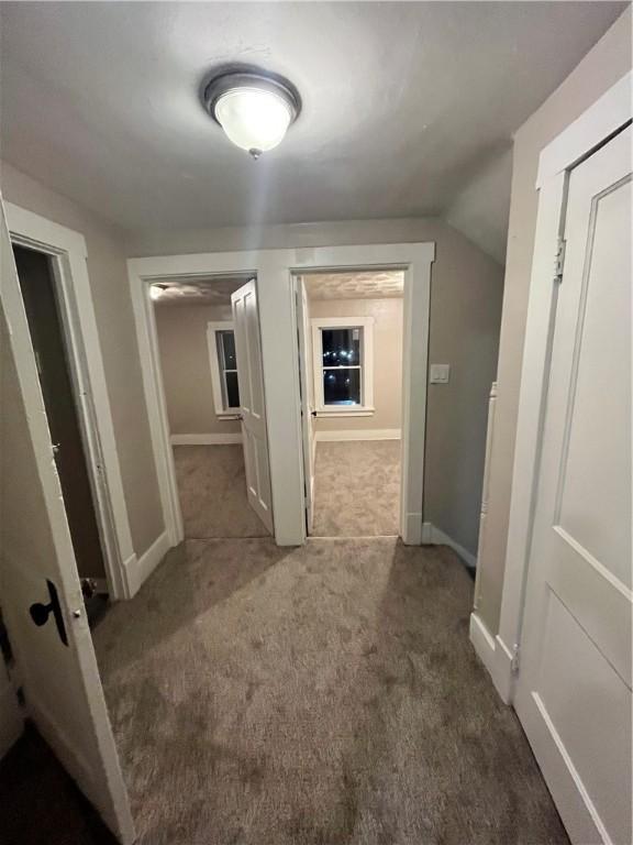 hall with lofted ceiling and dark carpet