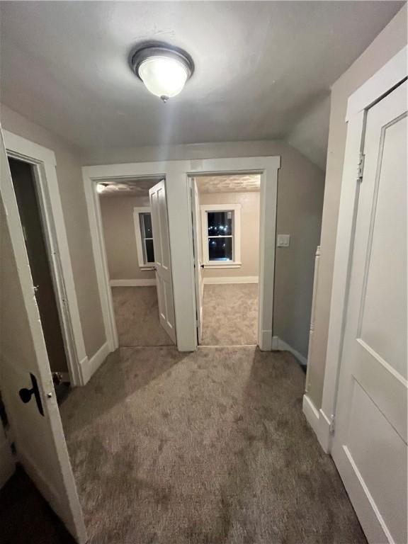 hallway with carpet, baseboards, and vaulted ceiling
