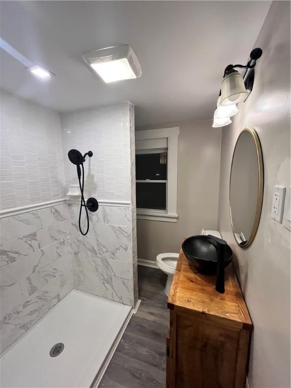 bathroom featuring hardwood / wood-style flooring, vanity, a tile shower, and toilet