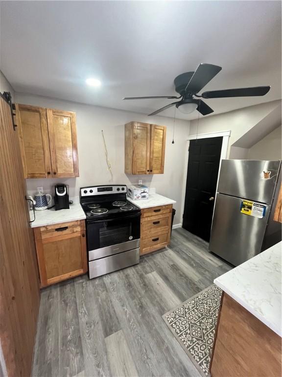 kitchen with appliances with stainless steel finishes, a ceiling fan, light wood-style flooring, light countertops, and brown cabinets