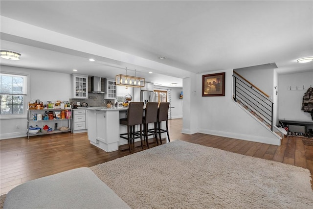 kitchen with pendant lighting, wall chimney exhaust hood, white cabinets, a breakfast bar, and a center island