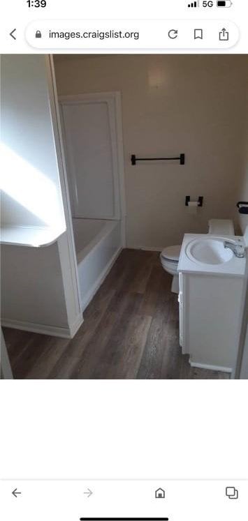 bathroom featuring toilet, vanity, a tub to relax in, and hardwood / wood-style flooring