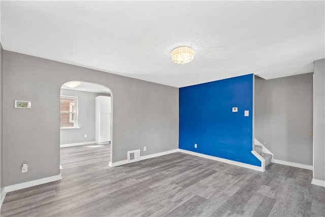 empty room featuring arched walkways, stairs, wood finished floors, and visible vents