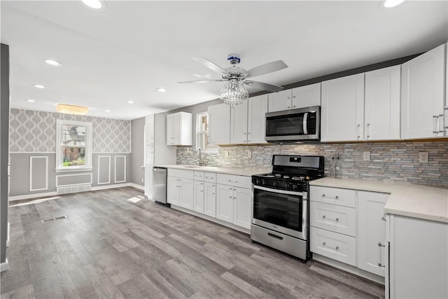 kitchen featuring wallpapered walls, white cabinetry, appliances with stainless steel finishes, and light wood finished floors