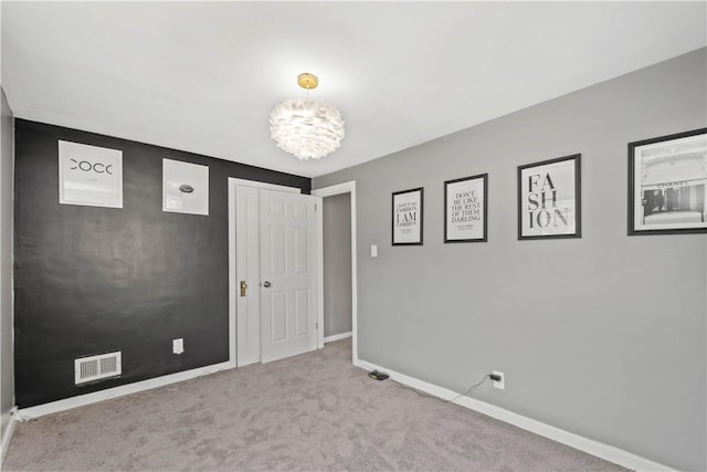 empty room with a chandelier, carpet, visible vents, and baseboards