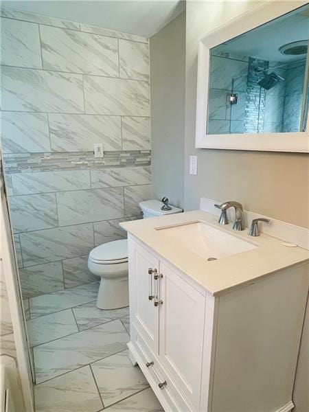 bathroom with marble finish floor, a tile shower, vanity, and toilet