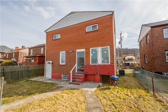 back of property featuring entry steps, brick siding, a lawn, and a fenced backyard