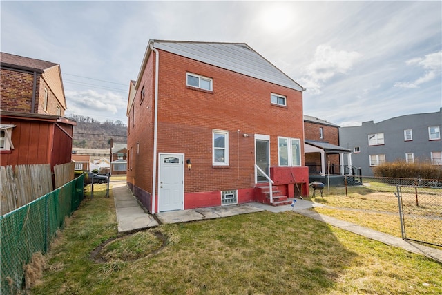 rear view of property with entry steps, a yard, fence, and brick siding