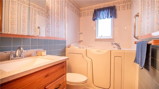 bathroom with a tub to relax in, vanity, tile walls, and toilet