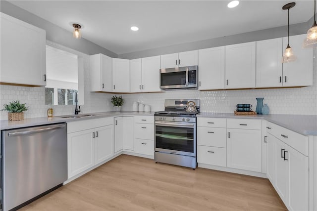 kitchen with pendant lighting, appliances with stainless steel finishes, white cabinetry, sink, and light hardwood / wood-style flooring