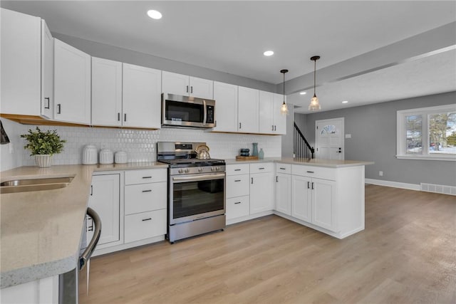 kitchen featuring white cabinets, hanging light fixtures, appliances with stainless steel finishes, and kitchen peninsula