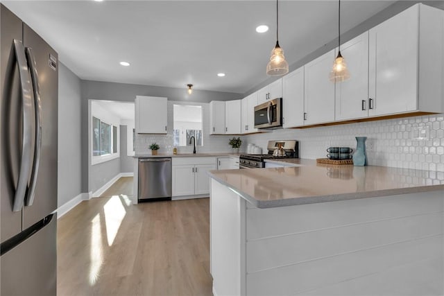 kitchen featuring pendant lighting, appliances with stainless steel finishes, white cabinetry, sink, and kitchen peninsula