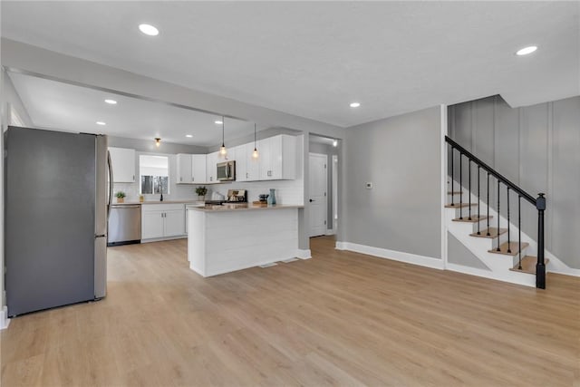 kitchen featuring decorative light fixtures, backsplash, light wood-type flooring, appliances with stainless steel finishes, and white cabinets