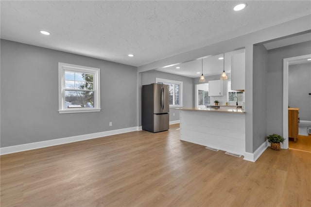 kitchen with white cabinetry, light wood-type flooring, hanging light fixtures, stainless steel refrigerator, and sink